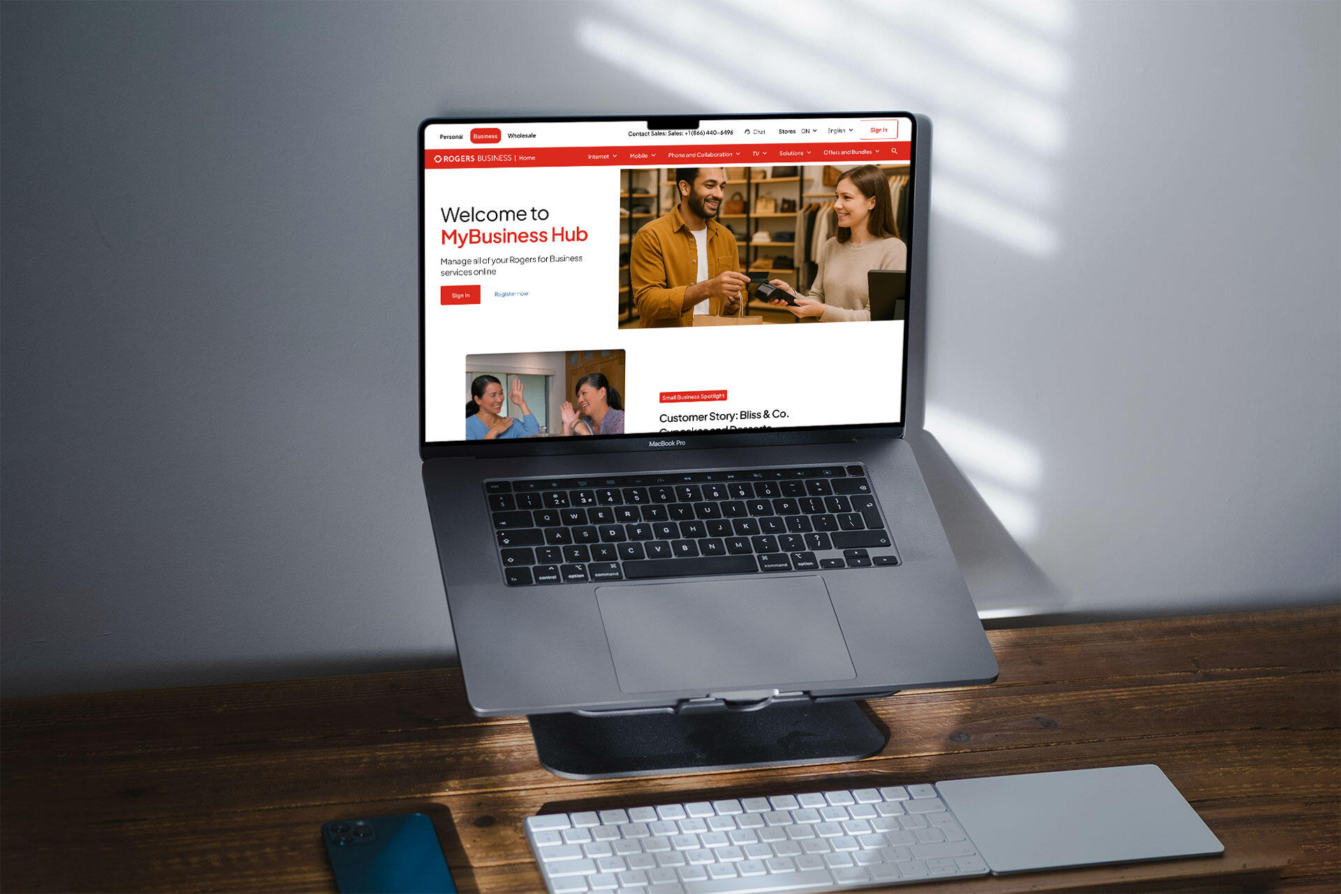 A laptop on a stand showing Rogers Business reimagined landing page in a room with a white wall and wooden desk.