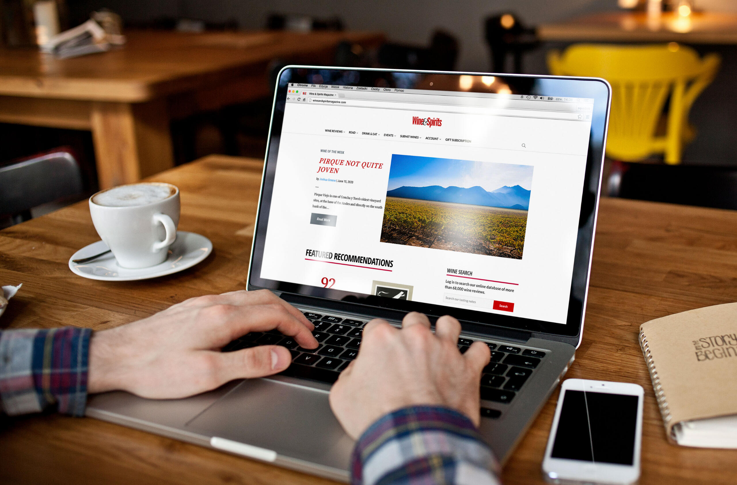Person's hands using a laptop visiting Wine & Spirits' website at a coffee shop.