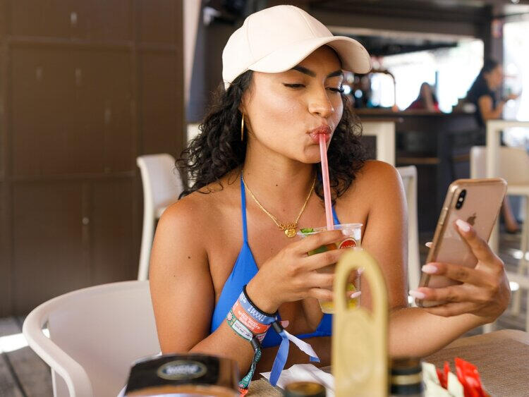 Woman taking a selfie with her smartphone while drinking something with a pink straw.